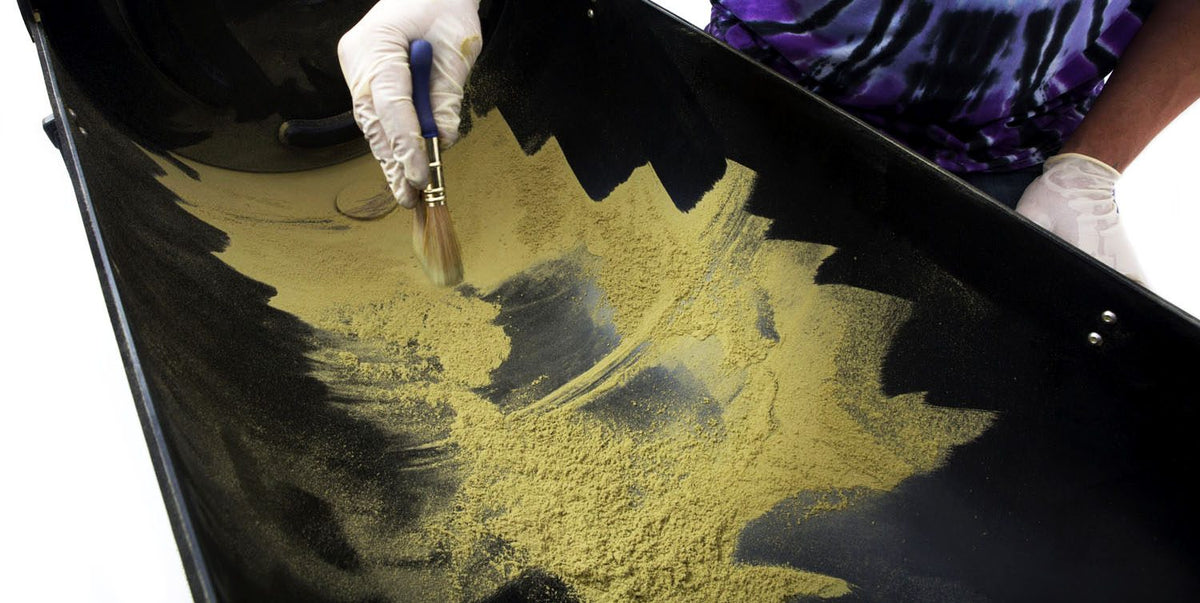 Gloved hand brushing golden kief from the collection tray of an Original Resinator