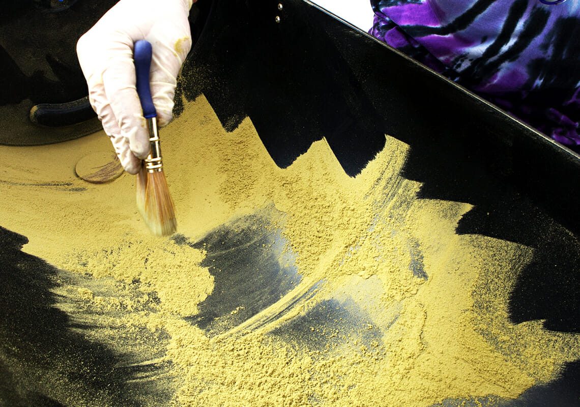 Gloved hand brushing collected golden trichomes and kief from the black collection tray of an Original Resinator